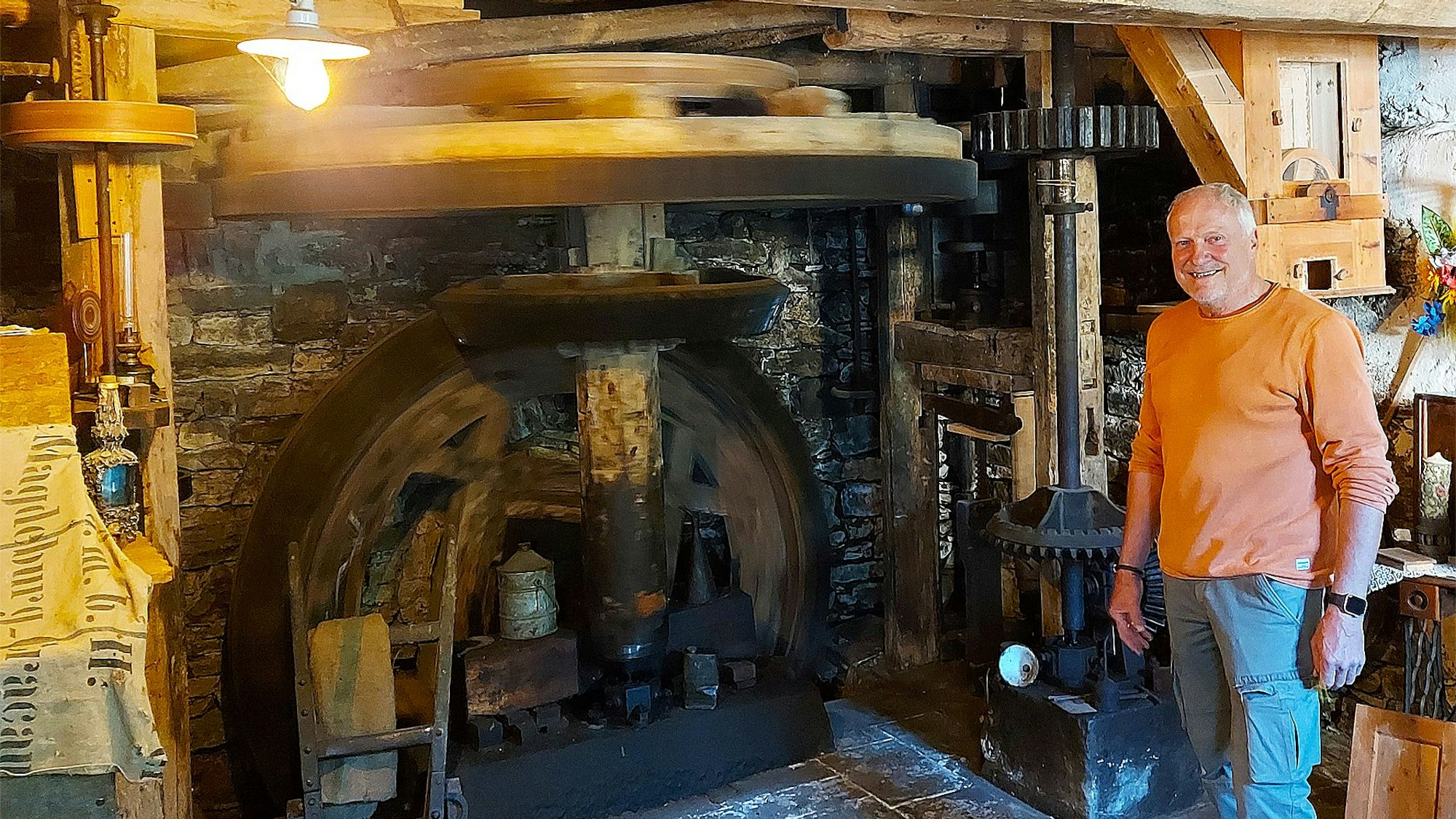 Walfried Heinen steht lächelnd in der historischen Mühle Falkenstein in Eiserfey. Eine Deckenlampe erleuchtet den Raum.