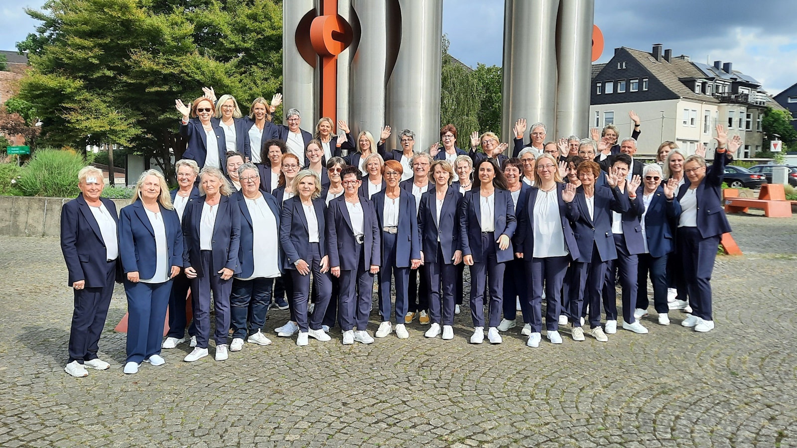 Ein Frauenchor posiert vor einer Stahlskulptur.