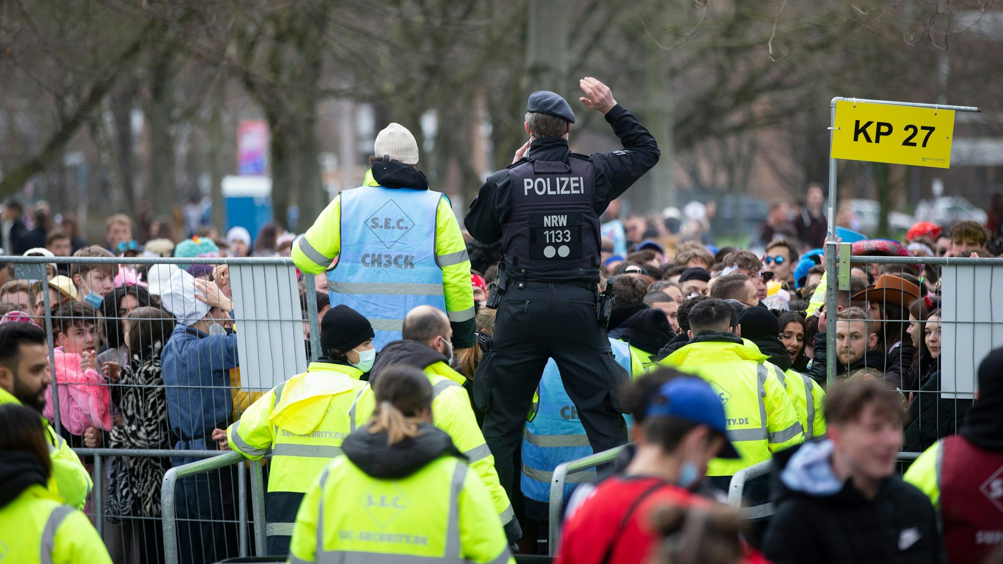 Sicherheitskräfte stehen mit leuchtenden Westen an einem Gitter. Ein Polizist steht auf dem Gitter.