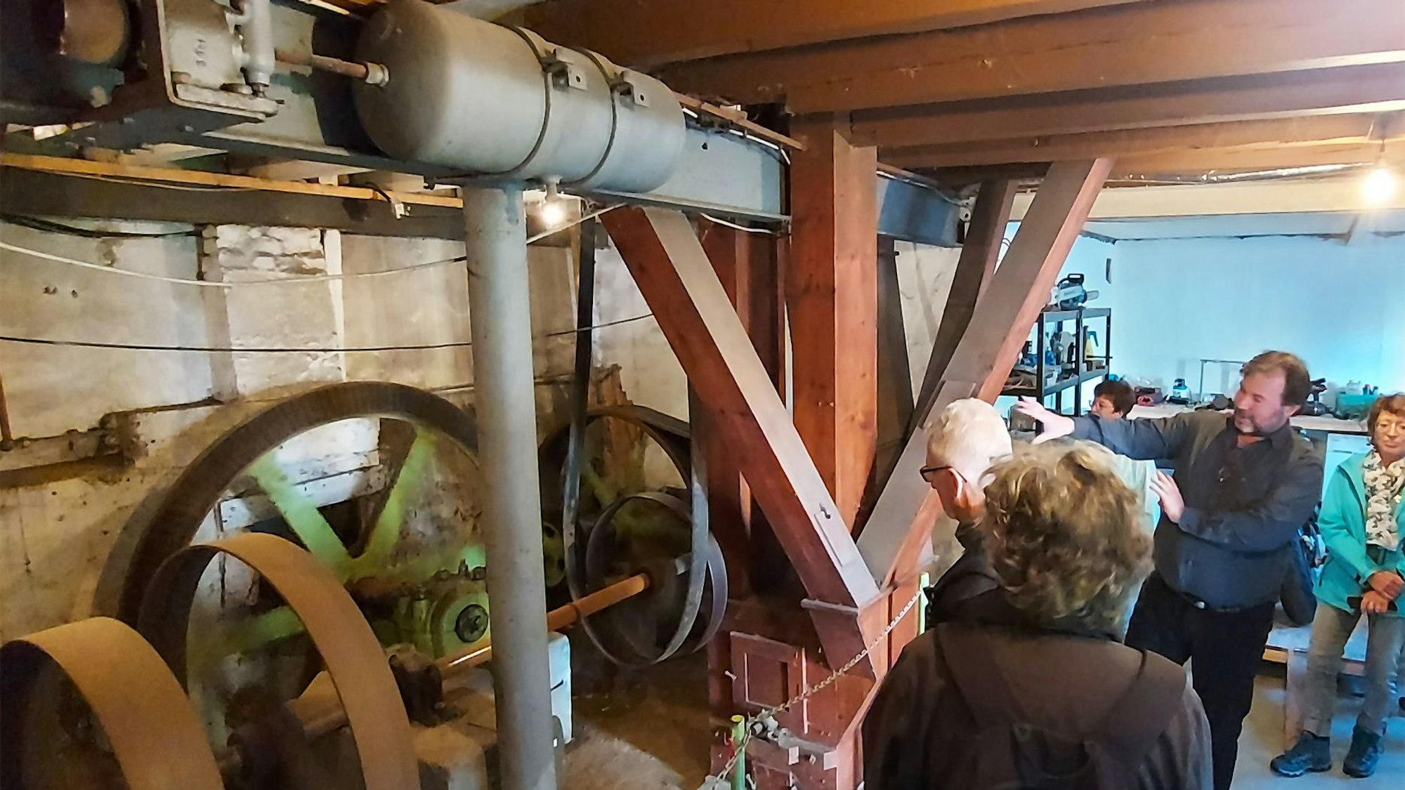 Der Eigentümer der Hauserbachmühle, Wolfgang Pütz, erklärt Besucherinnen und Besuchern die Technik. Er zeigt auf Räder, Riemen und andere Teile der historischen Anlage.