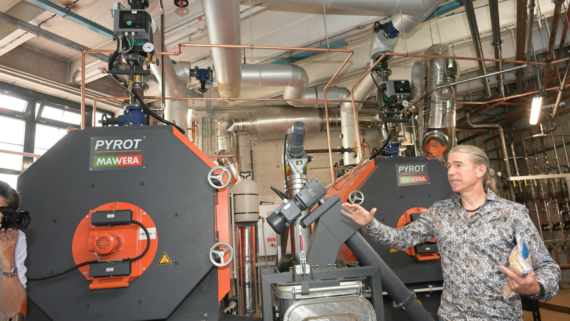 Marco Preußer steht neben einem der beiden meterhohen Heizkessel aus schwarzem Stahl im Keller der Heizungszentrale.