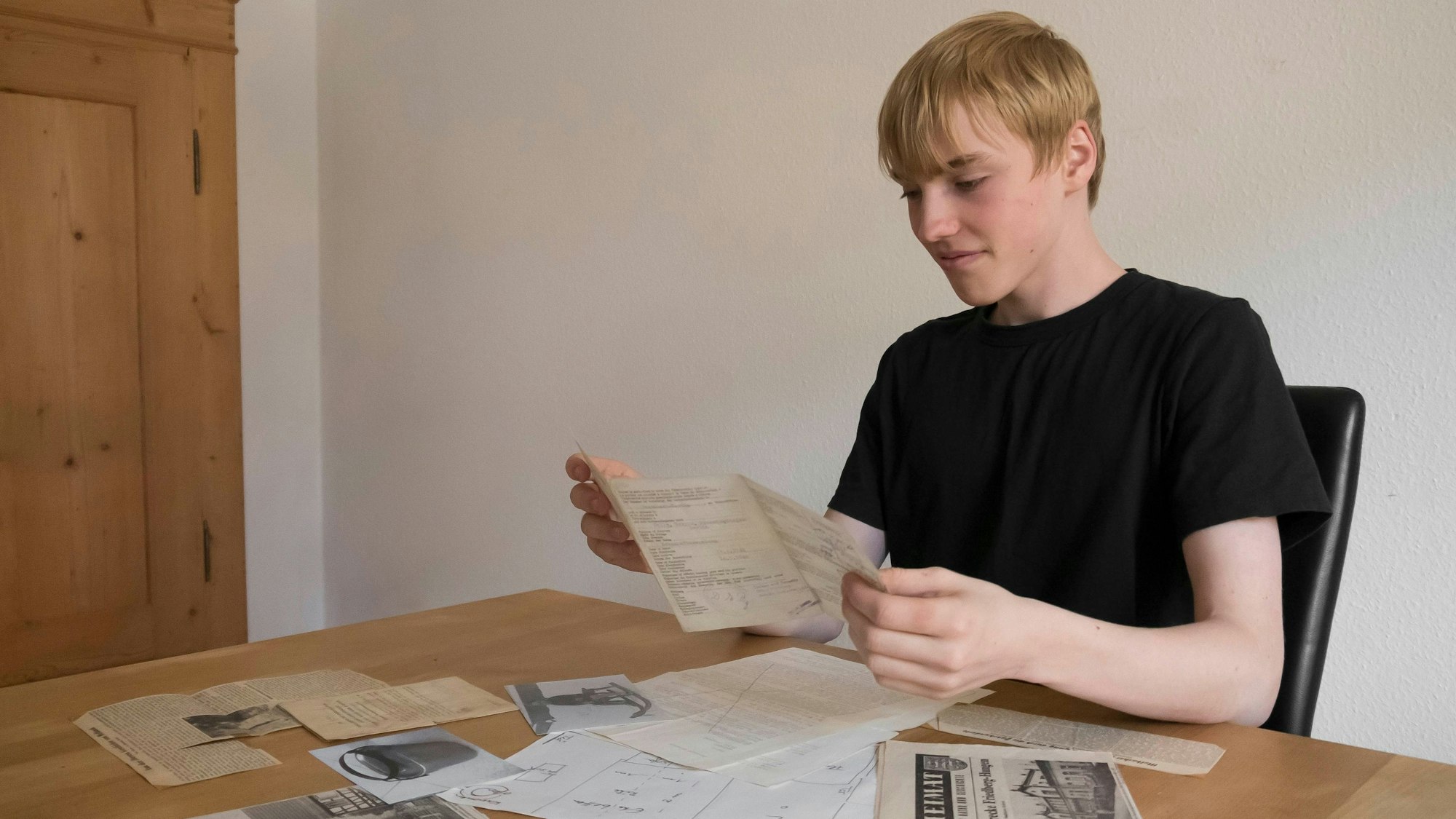 Ein junger Mann sitzt an einem Tisch und sichtet alte Dokumente.