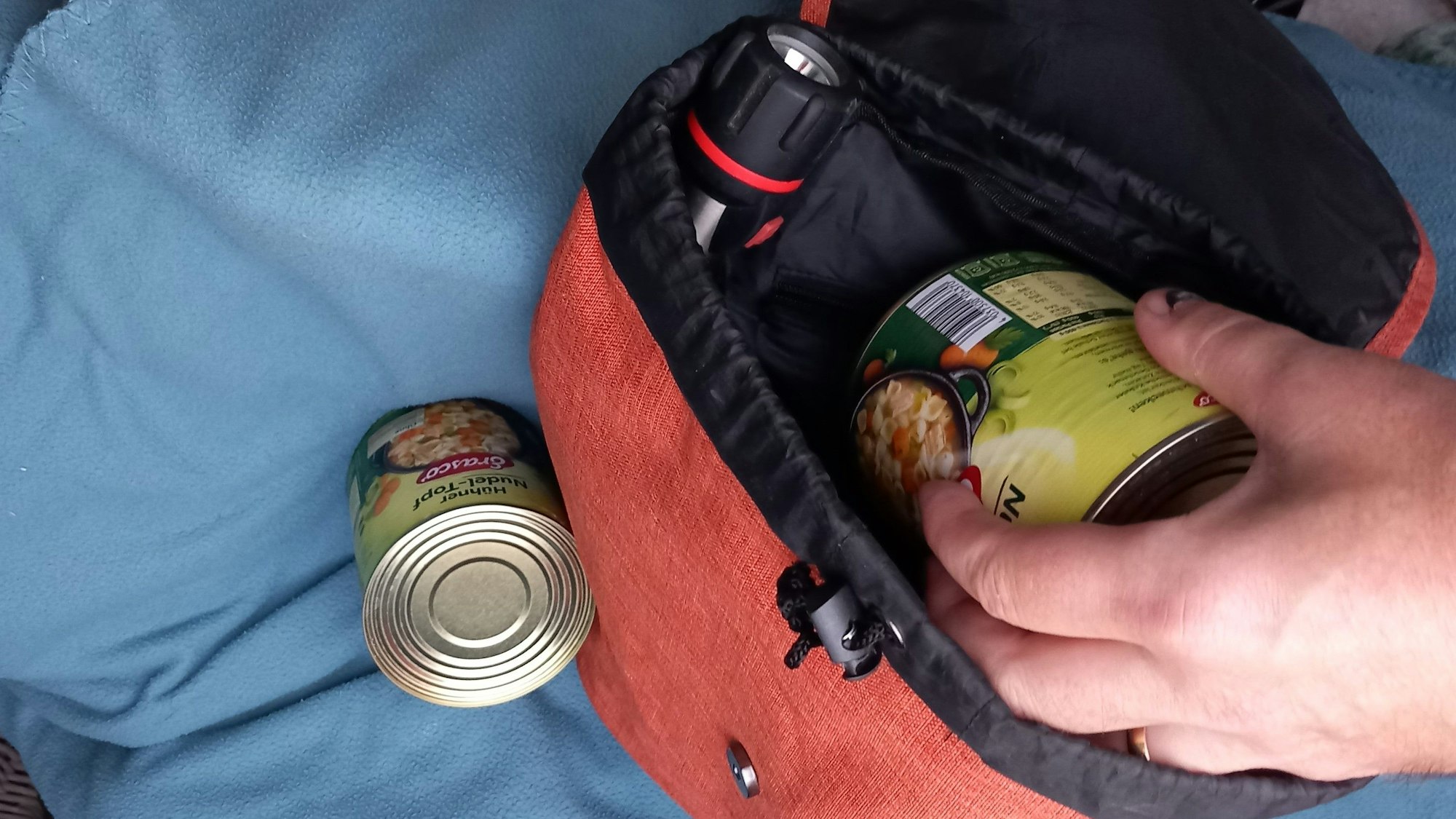Ein Notfallrucksack wird mit Konserven und Taschenlampe bestückt.