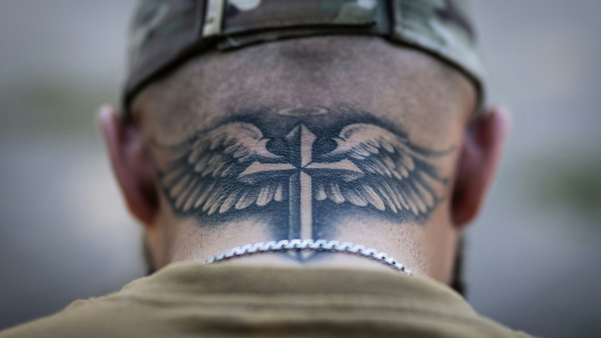 Ein Mann hat ein von Engelsflügeln gehaltenes Kreuz in Schwertform auf seinen Nacken tätowiert.