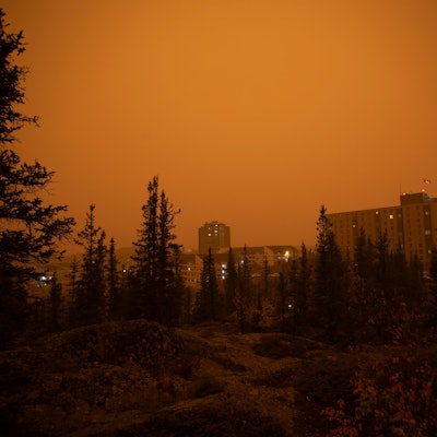 Starker Rauch von Waldbränden im Norden von Alberta und British Columbia zieht über die Stadt Yellow Knife im kanadischen Bundesstaat Northwest Territories hinweg. Die Gebäude und der Wald sind in einen gelben und orangefarbenen Nebel gehüllt.