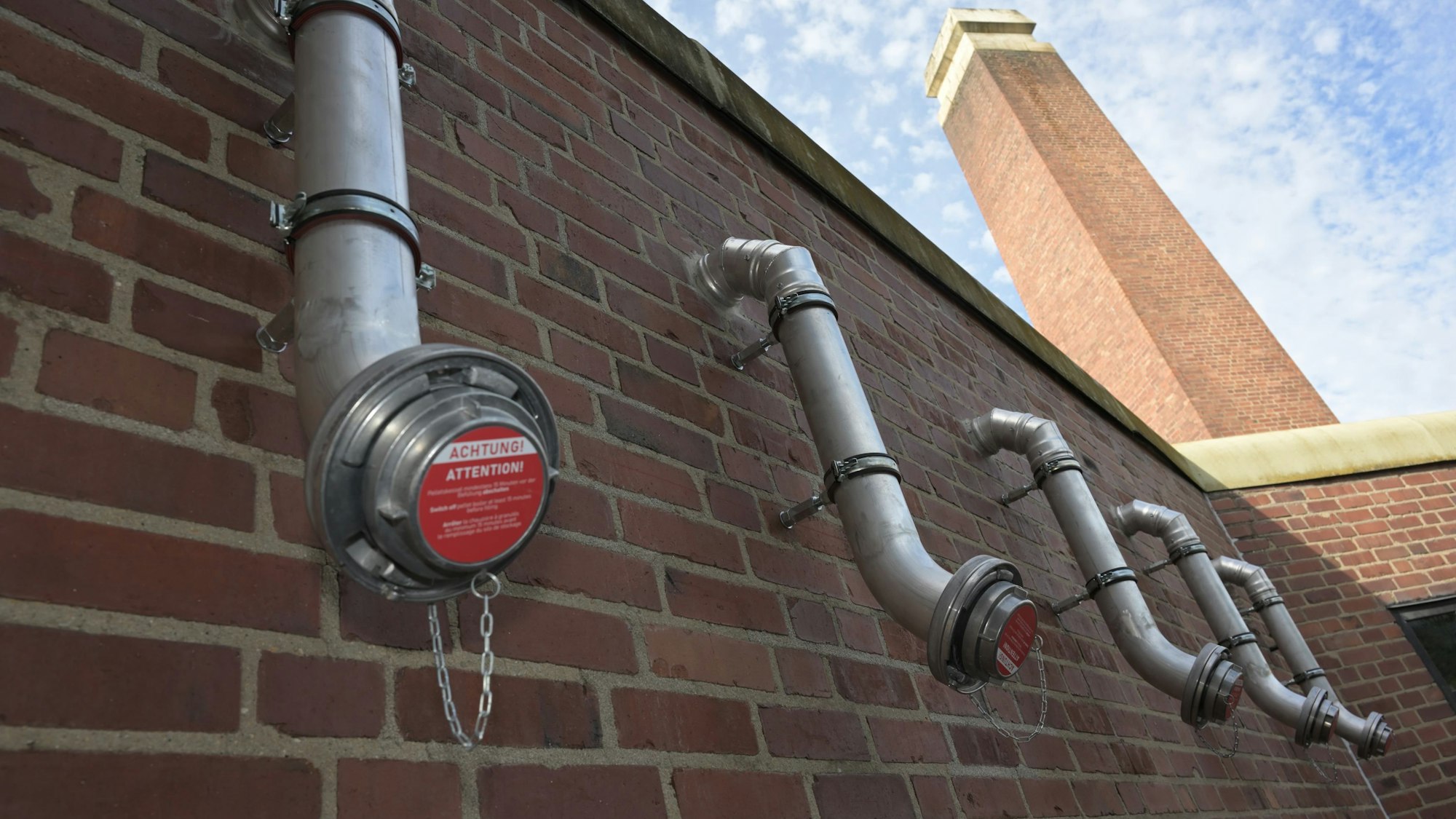 Fünf Aluminiumstutzen, nebeneinander angebracht, ragen aus einer Backsteinwand.