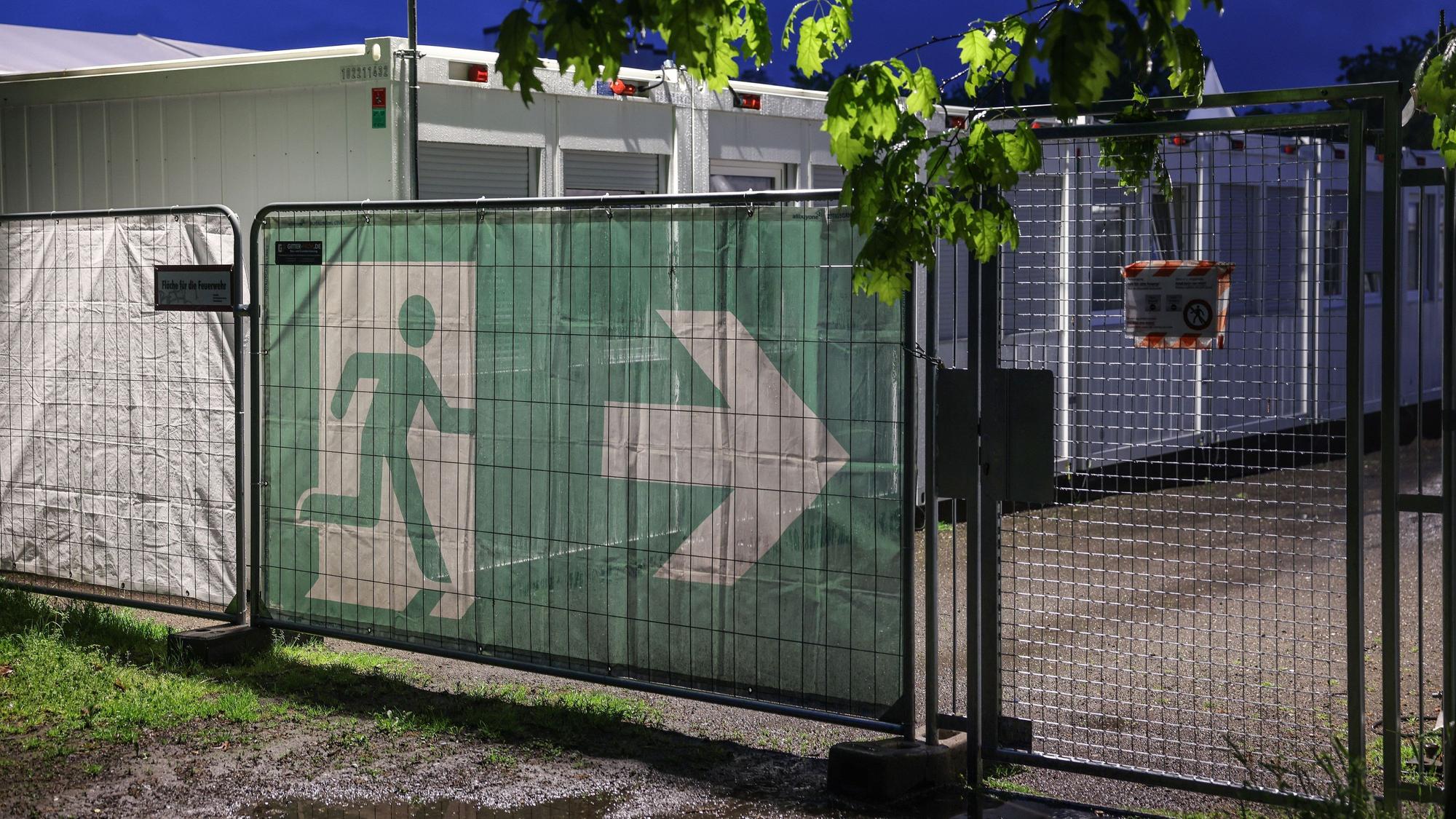 10.05.2023, Nordrhein-Westfalen, Köln: Ein Transparent mit dem Symbol für den Fluchtweg hängt vor Wohncontainer der kommunalen Erstaufnahmeeinrichtung in Köln-Zollstock. Bund und Länder suchen bei einem Spitzentreffen in Berlin nach Lösungen im Streit über die Aufteilung der Kosten für die Versorgung von Flüchtlingen. (Zu dpa: «Gipfel berät über Flüchtlingsfrage») Foto: Oliver Berg/dpa +++ dpa-Bildfunk +++