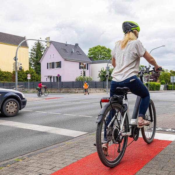Eine Frau steht mit ihrem Fahrrad an einer Ampel.