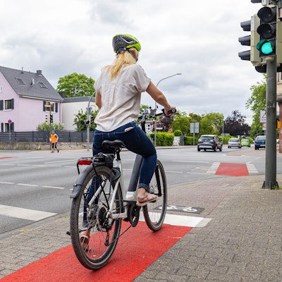 Eine Frau steht mit ihrem Fahrrad an einer Ampel.