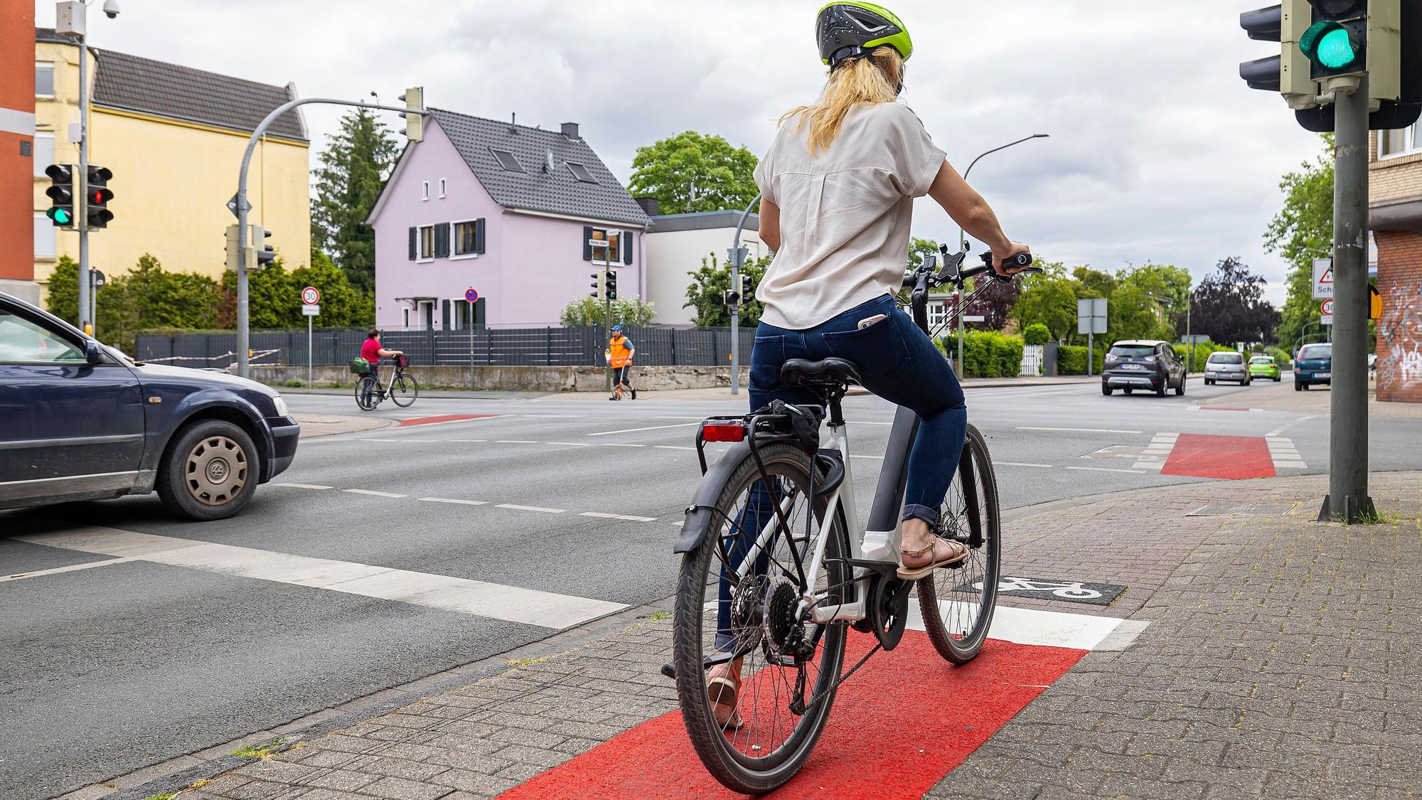 Eine Frau steht mit ihrem Fahrrad an einer Ampel.
