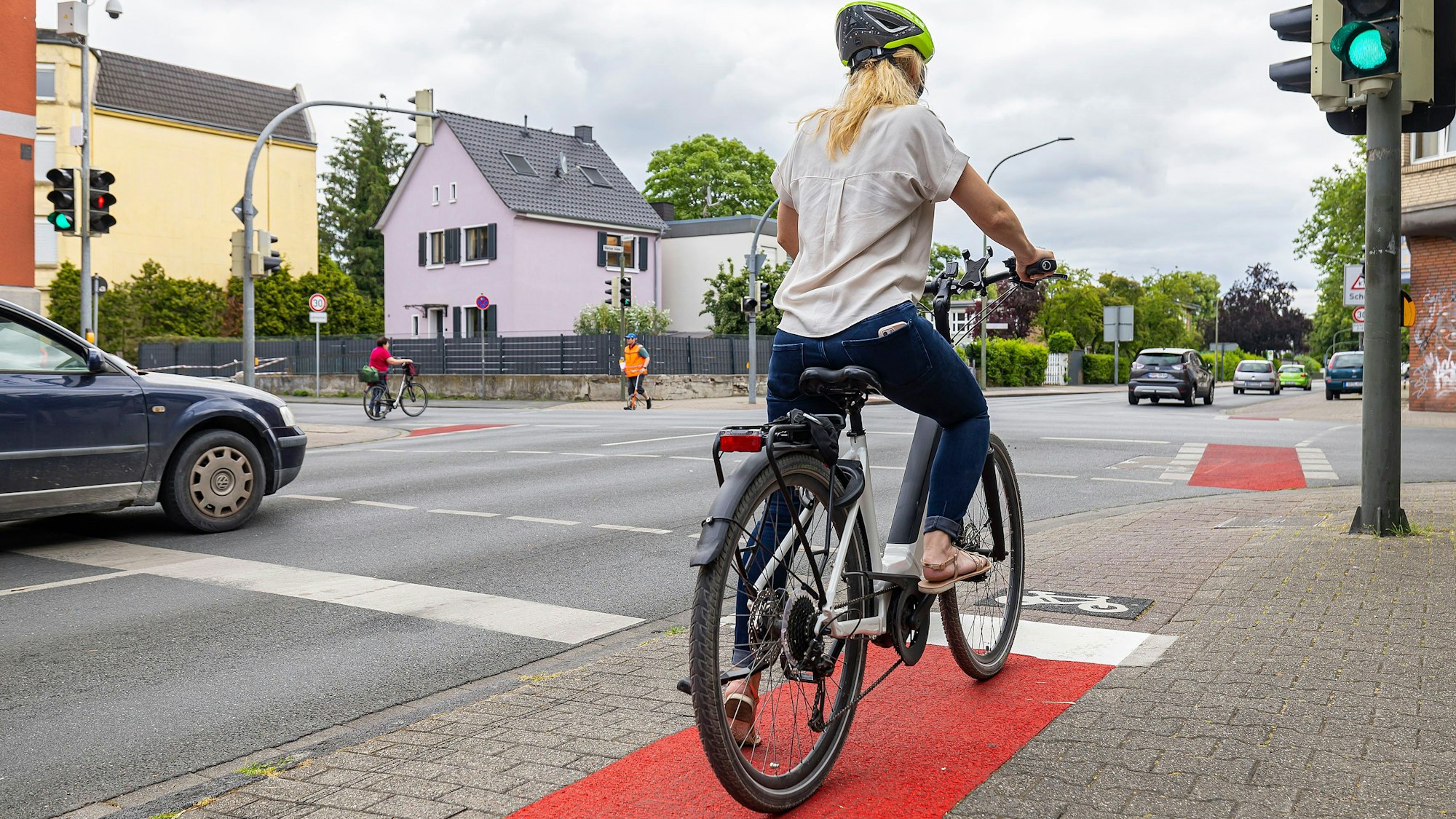 Eine Frau steht mit ihrem Fahrrad an einer Ampel.