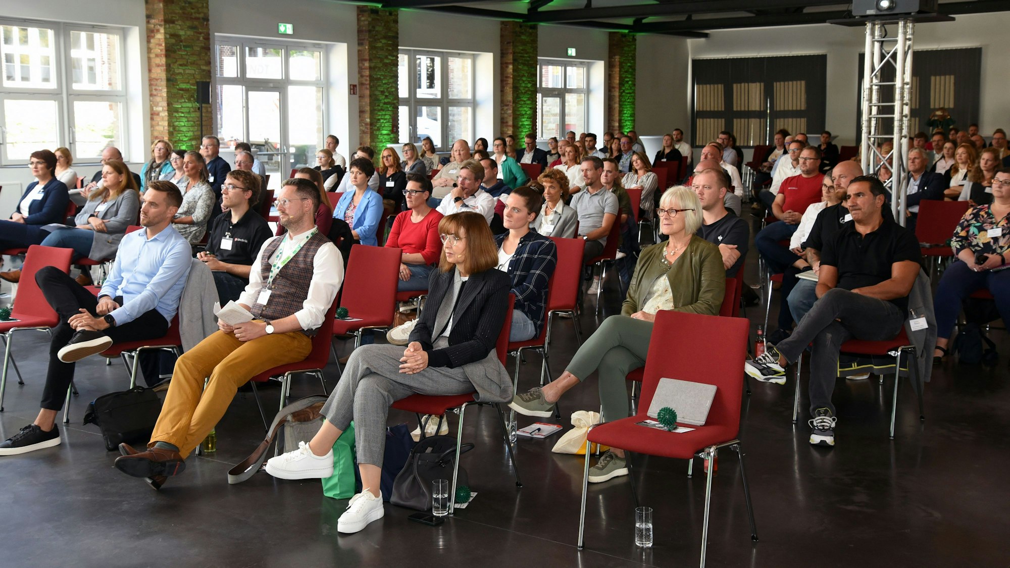 Ein Saal voll mit Menschen, die auf Stühlen sitzen und einem Vortrag zuhören.