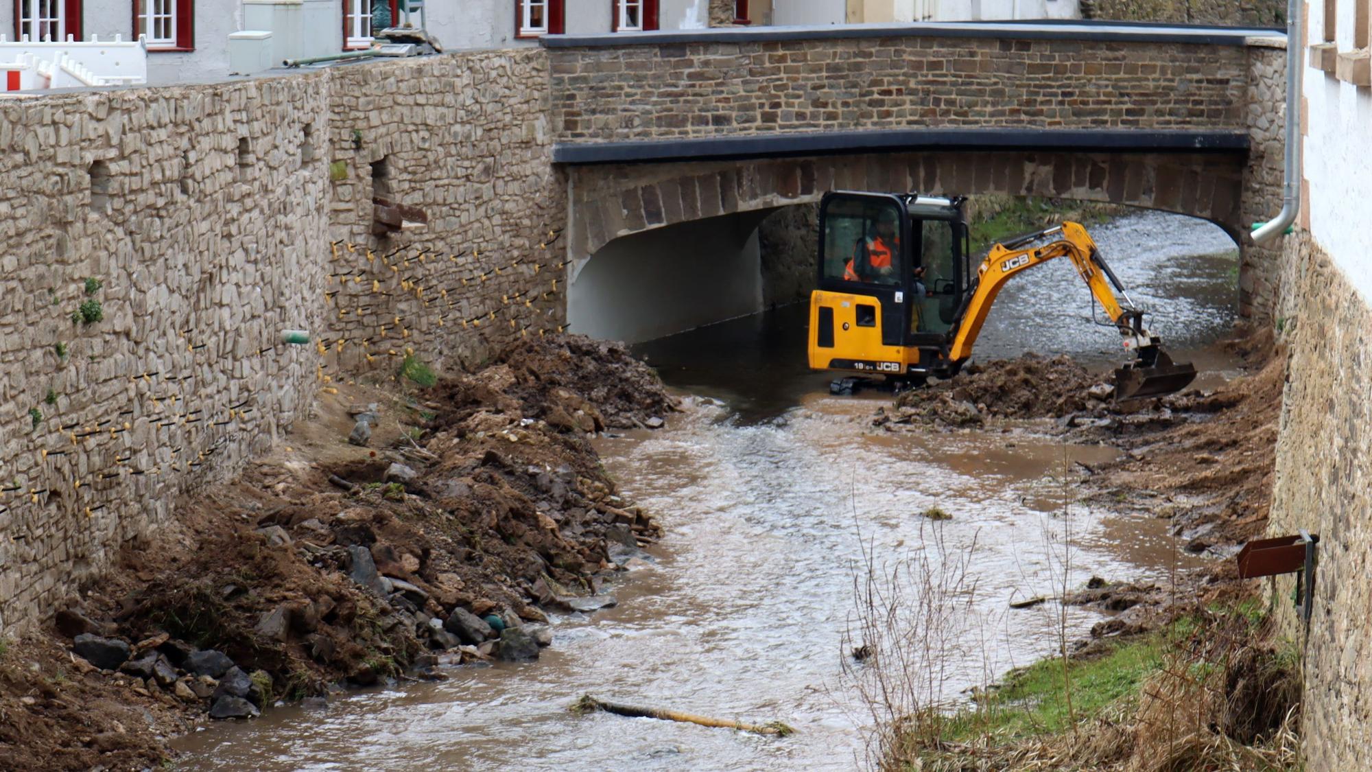 Ein Bagger steht in der Erft in Bad Münstereifel. Zu sehen sind auch die wieder aufgebauten Erftmauern.