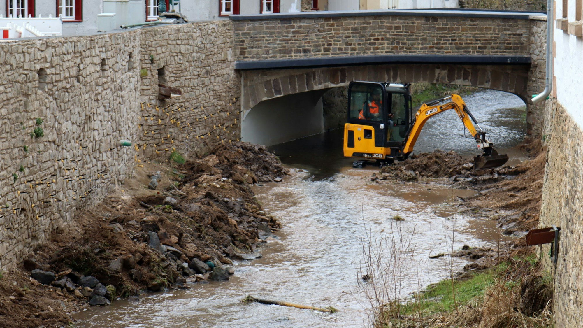 Ein Bagger steht in der Erft in Bad Münstereifel. Zu sehen sind auch die wieder aufgebauten Erftmauern.