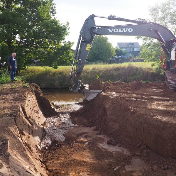 Ein Bagger schaufelt Erde weg, sodass Wasser in eine Rinne fließt.