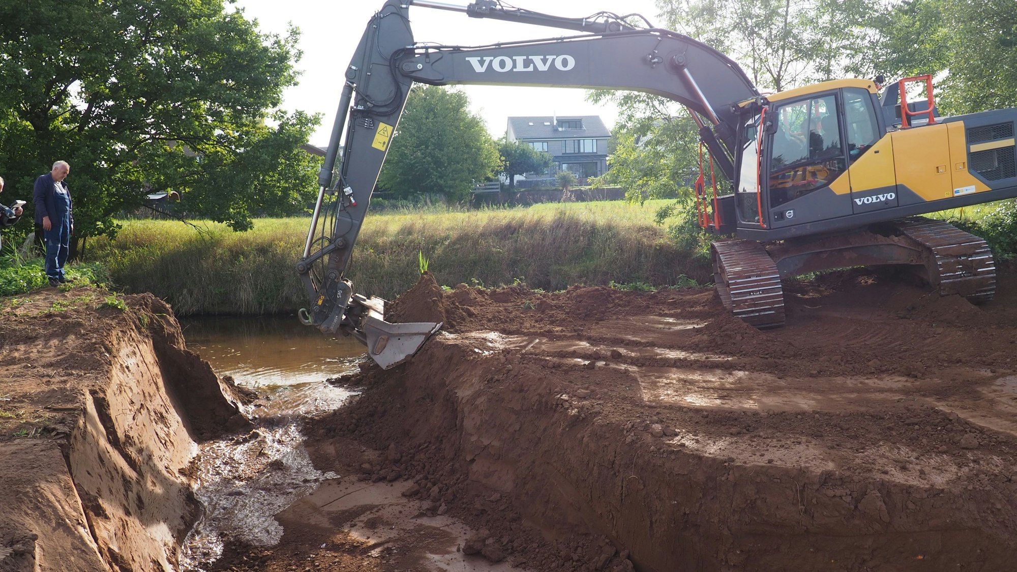Ein Bagger schaufelt Erde weg, sodass Wasser in eine Rinne fließt.