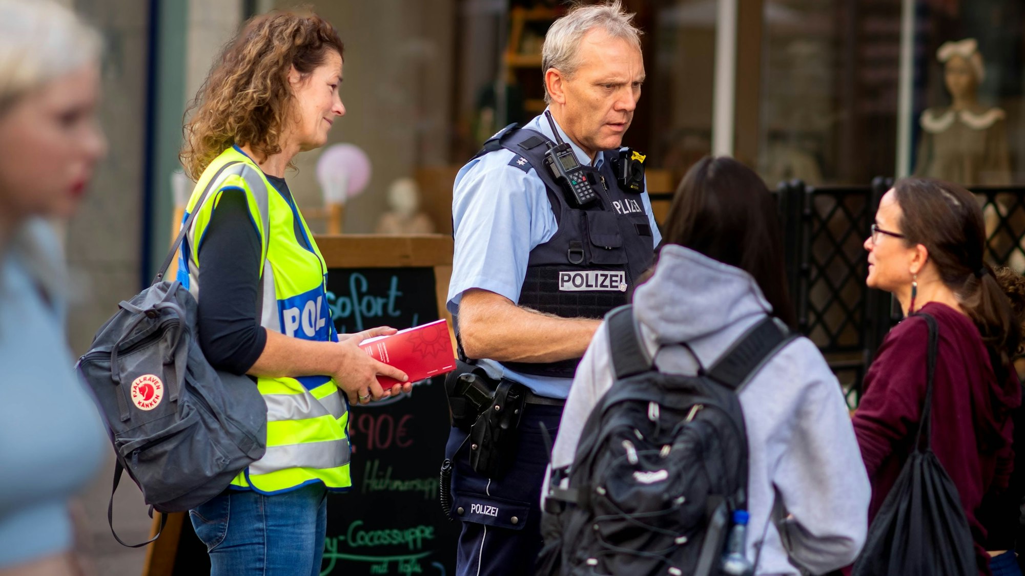 Das Bild zeigt Markus Braun in Polizeiuniform und Simone Becker in gelber Warnweste im Gespräch mit zwei Frauen.