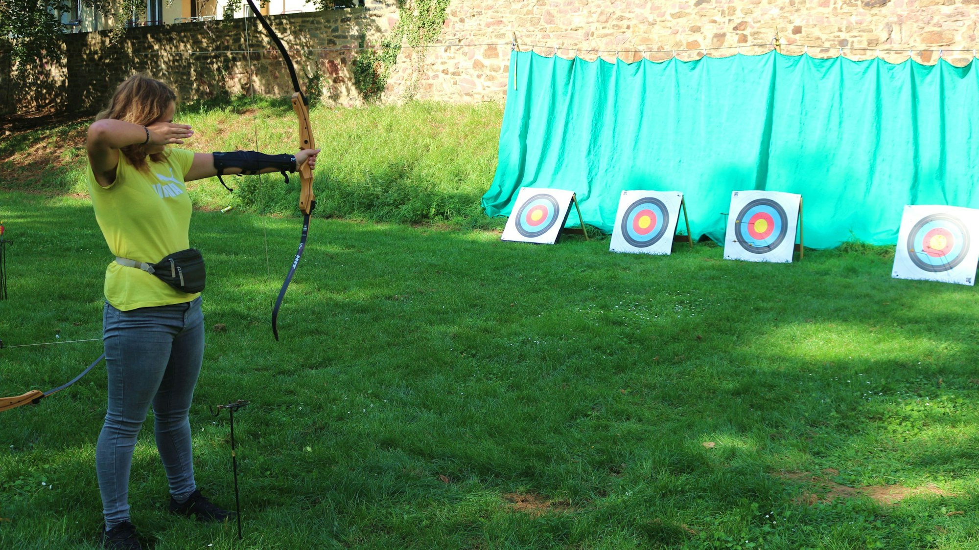 Ronja Krobs hält einen Bogen in der Hand. Vor ihr stehen in ein paar Metern Entfernung Zielscheiben auf dem Boden.