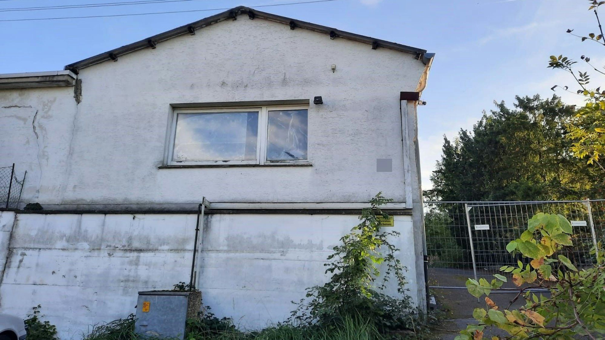 Ein heruntergekommenes Gebäude. Ein Gitterbauzaun versperrt den Zugang zum Grundstück.