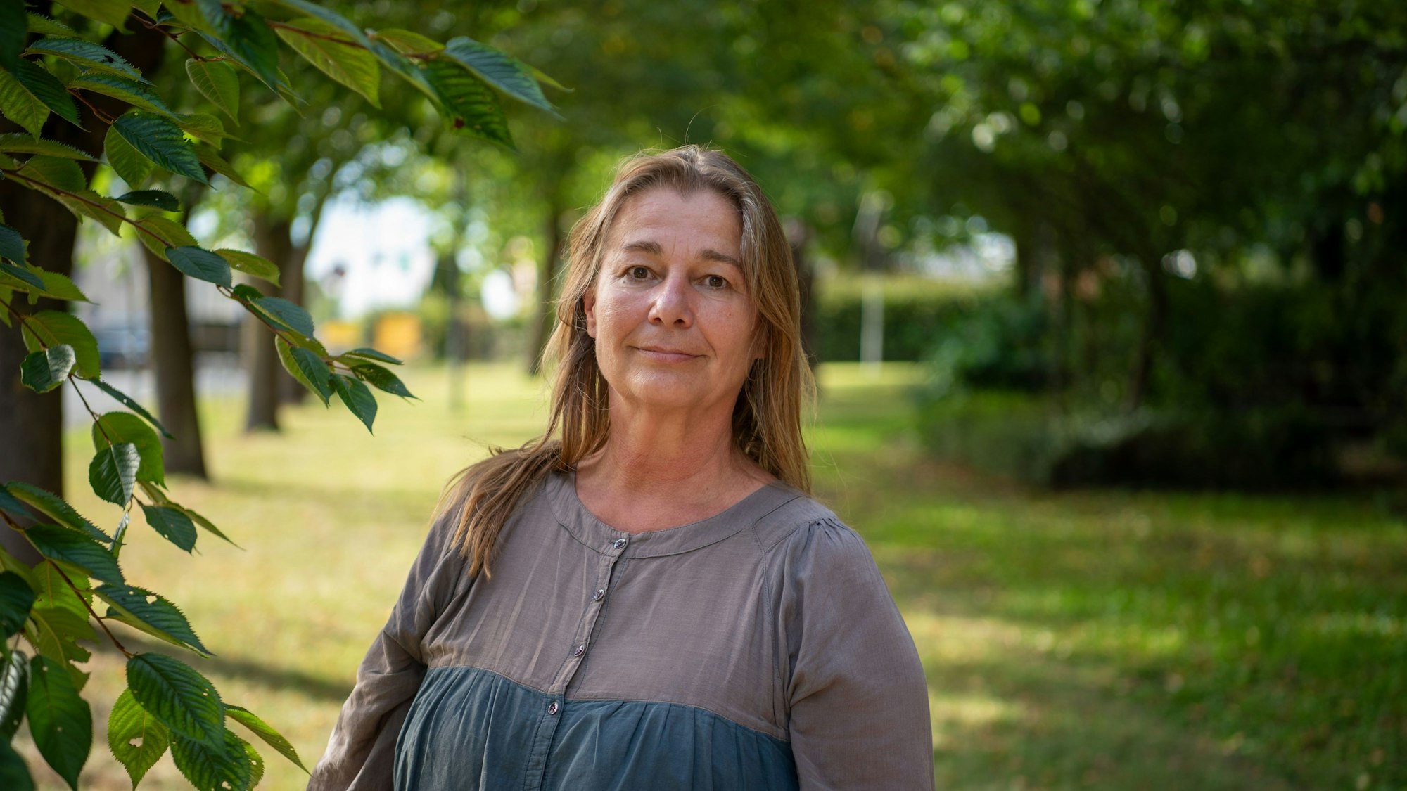 Die Künstlerin Alexandra Rix steht auf einer Wiese neben einem Baum.
