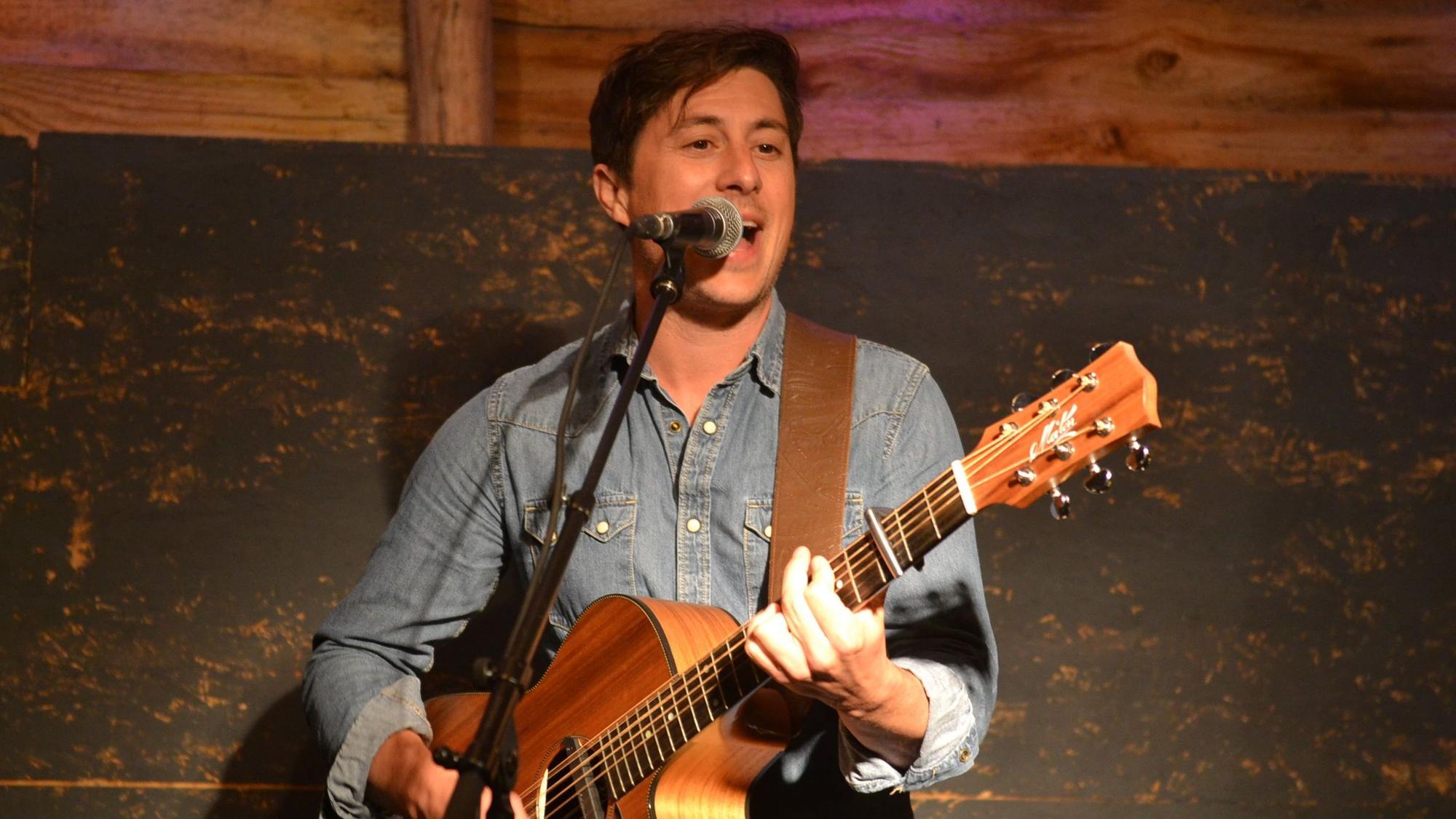 Der aus Australien stammende Musiker Jaimi Faulkner steht mit einer Gitarre am Mikrofon und singt.