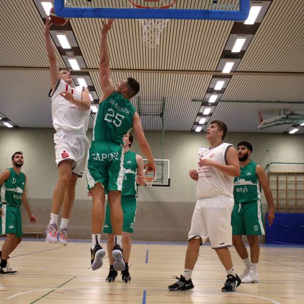 Basketballspielszene unter dem Korb: Ein Zülpicher Spieler steigt zum Sprungwurf hoch, ein Aachener Spieler blockt ihn.
