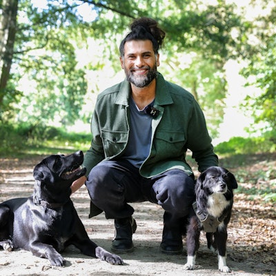 Hunde-Verhaltenstherapeut Masih Samin mit zwei Hunden auf einem Waldweg.