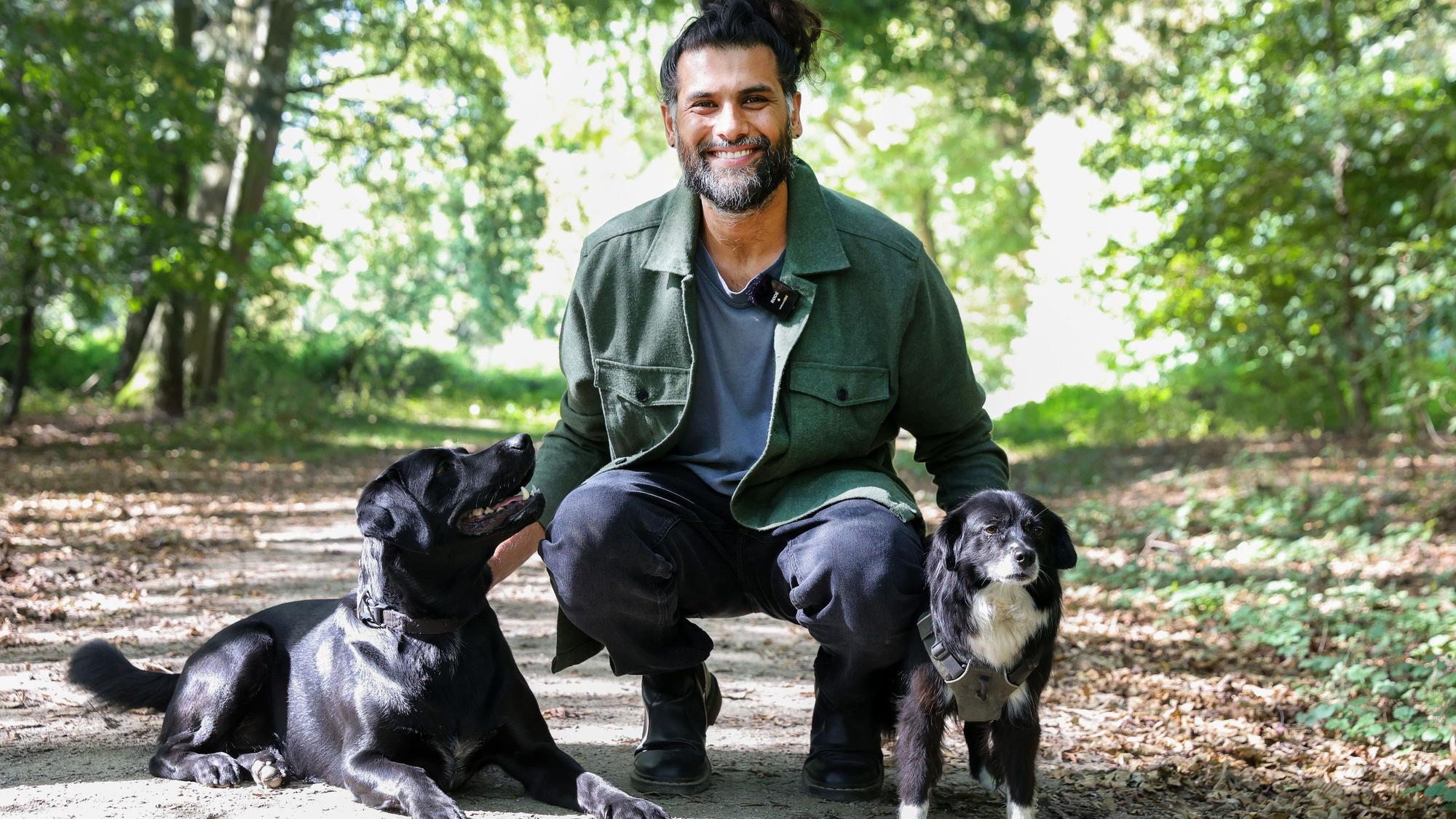 Hunde-Verhaltenstherapeut Masih Samin mit zwei Hunden auf einem Waldweg.