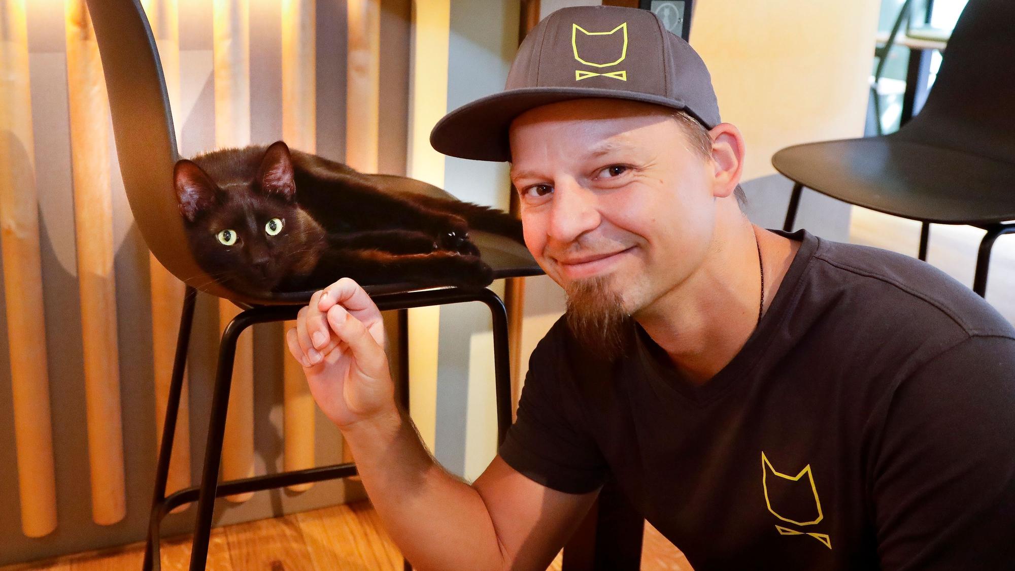 Michael Guddat, Tierpsychologe, Katzensitter und Katzenexperte, mit einer schwarzen Katze im Café Katzentempel in der Kölner Severinstrasse.