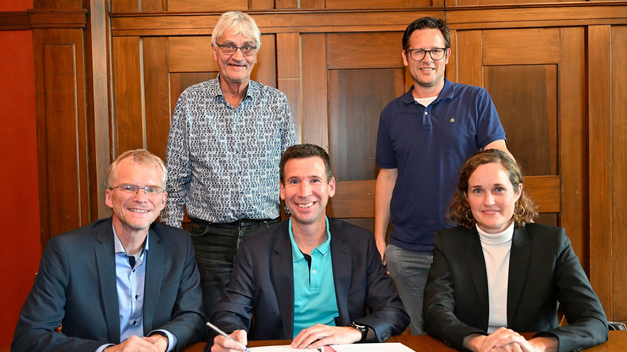 Am Tisch sitzen Bürgermeister Stein, Christian Metten und Jennifer Vollmer. Der Vertrag liegt vor ihnen. Hinter ihnen stehen Marco Häusling und Ron Woydowski.