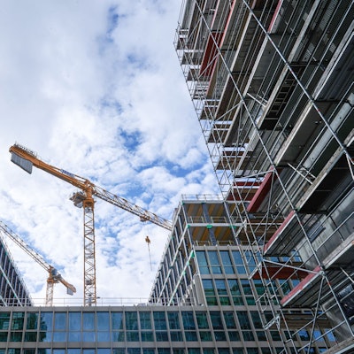 Zwei Baukräne stehen hinter einem Rohbau.