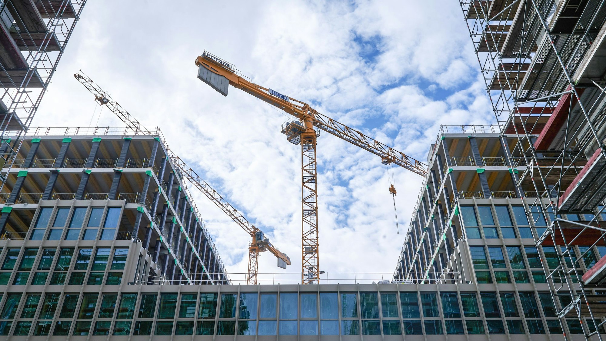 Zwei Baukräne stehen hinter einem Rohbau.
