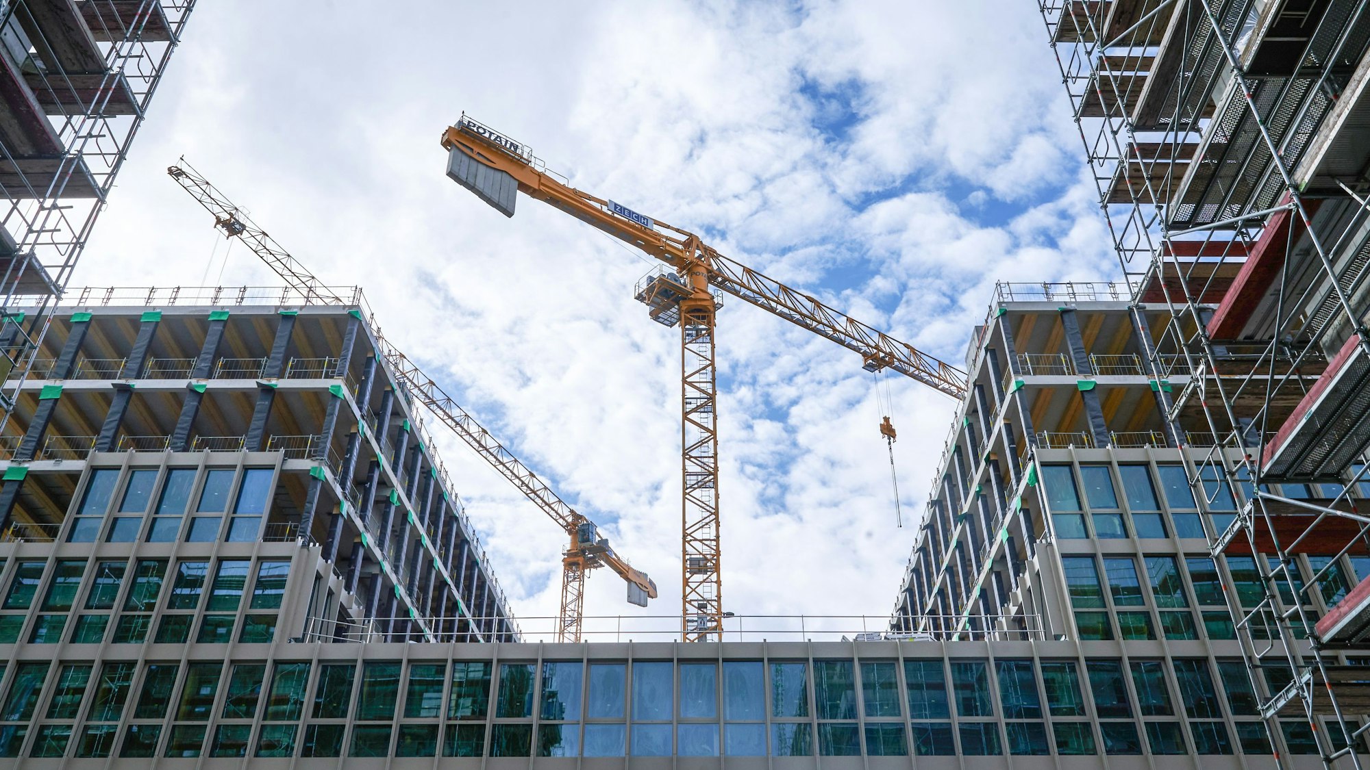 Zwei Baukräne stehen hinter einem Rohbau.