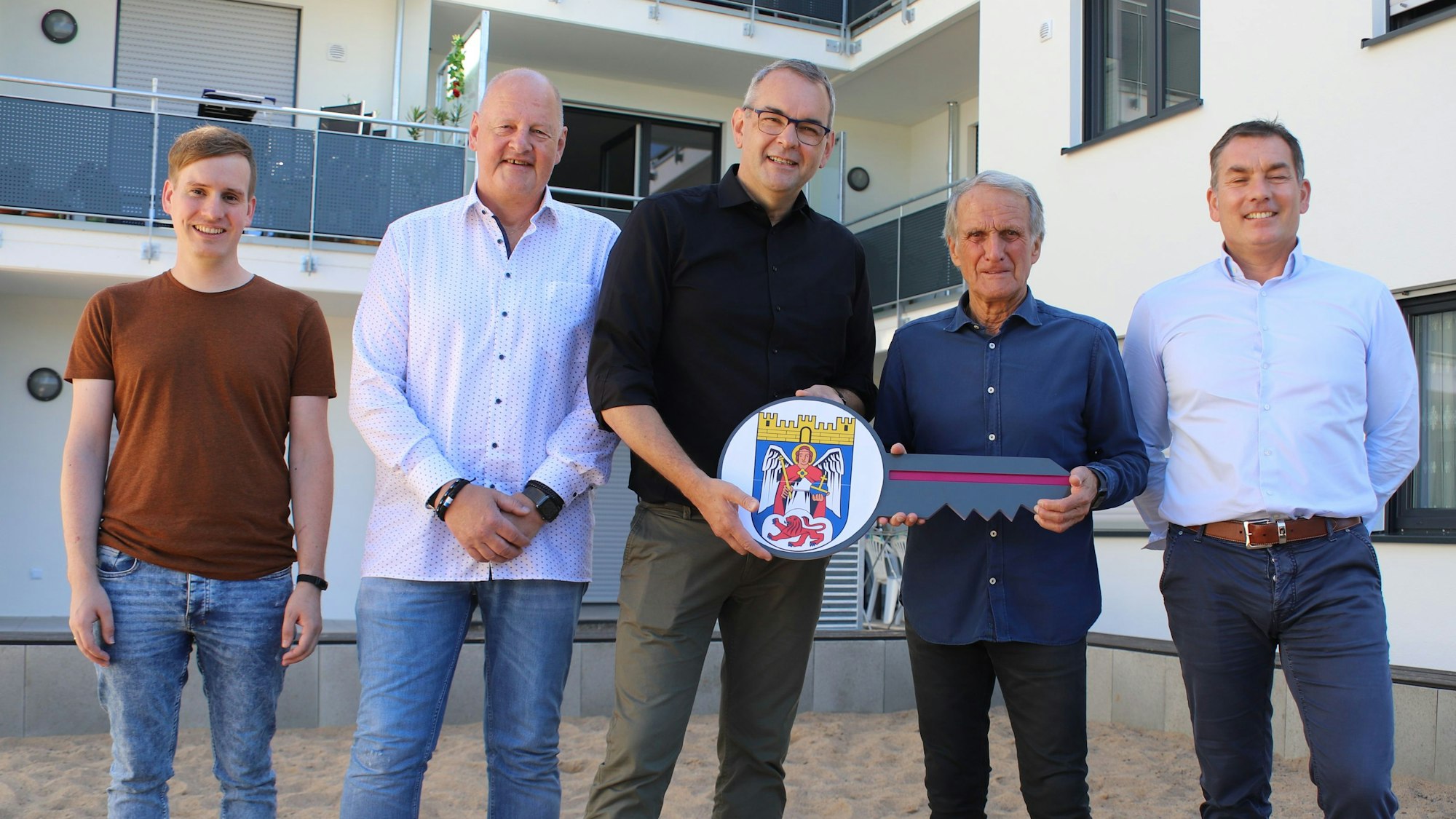 Wolfgang Overath mit einer Gruppe von anderen Männern vor einem neu gebauten Wohngebäude