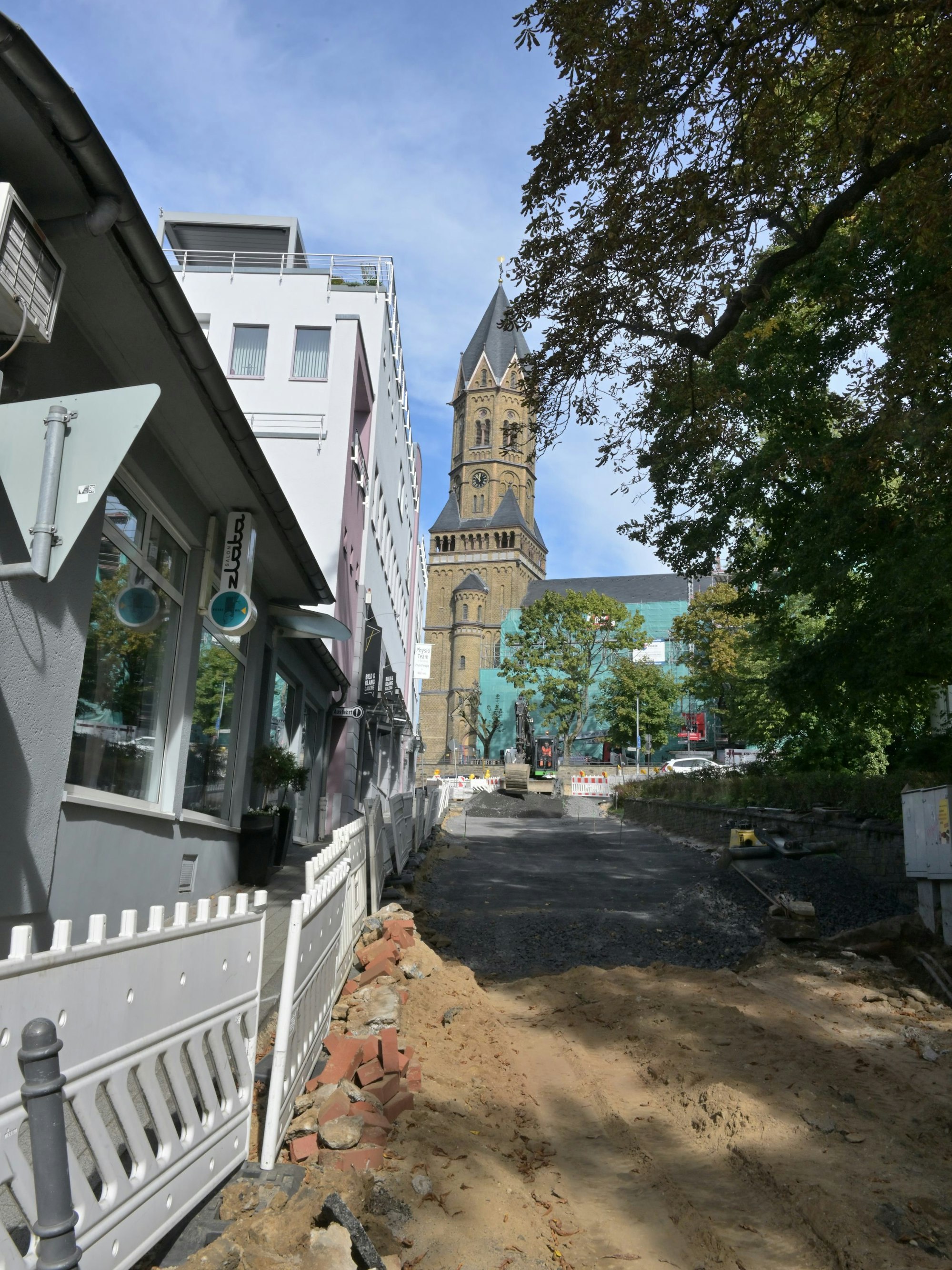 Bauzäune stehen vor offengelegten Straße. Am Rand ist ein kleiner Streifen Gehweg.