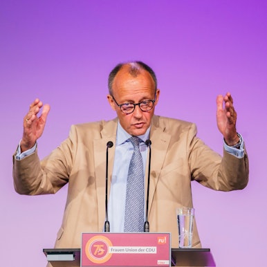 Der CDU-Vorsitzende Friedrich Merz hebt bei einer Rede beide Arme nach oben und gestikuliert vor einem Rednerpult.