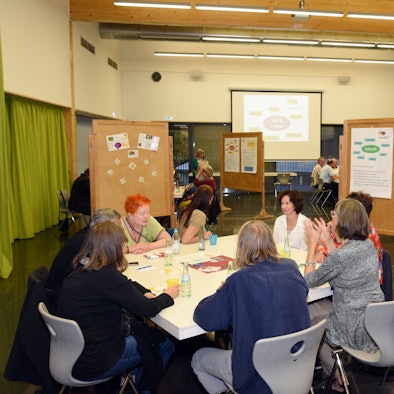 Ein Blick in den Saal, in dem Menschen an vier Tischen sitzen und diskutieren.