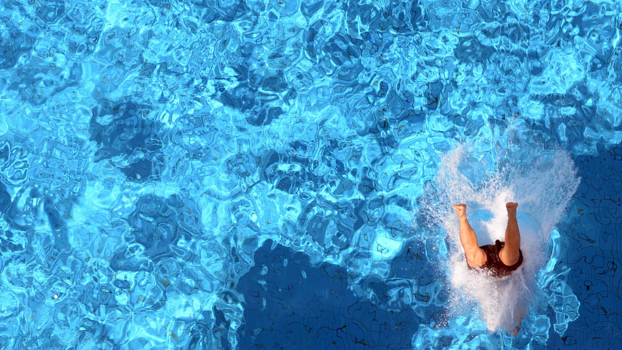 Ein Badegast springt kopfüber ins schillernd blaue Schwimmbecken.