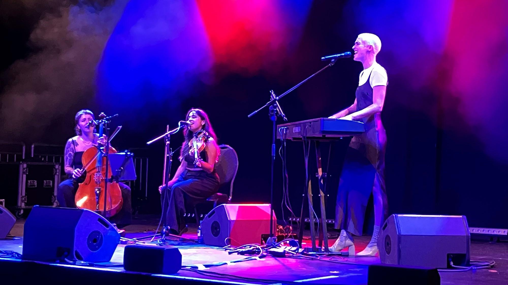 Drei Musikerinnen auf einer Bühne am Keyboard, Geige und Cello.