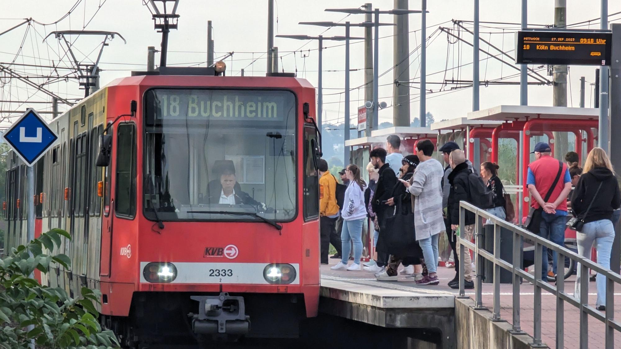 Das Foto zeigt Fahrgäste, die am Bahnsteig stehend, auf eine einfahrende Bahn warten.