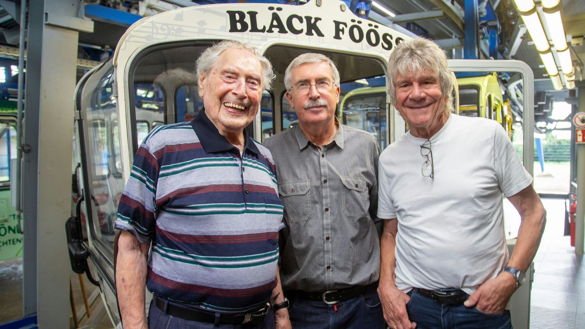 Vor einer Seilbahn-Kabine stehen Ludwig Sebus, Texter Manfred Schäfer und Bömmel Lückerath.
