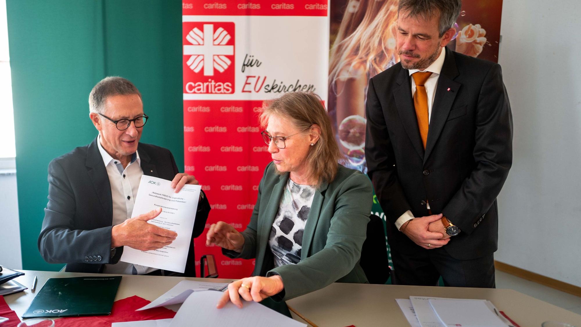 Das Bild zeigt Helmut Schneider, Regionaldirektor der AOK Rheinland/Hamburg, sowie Maria Surges-Brilon und Martin Jost vom Vorstand der Caritas bei der Vertragsunterschrift.
