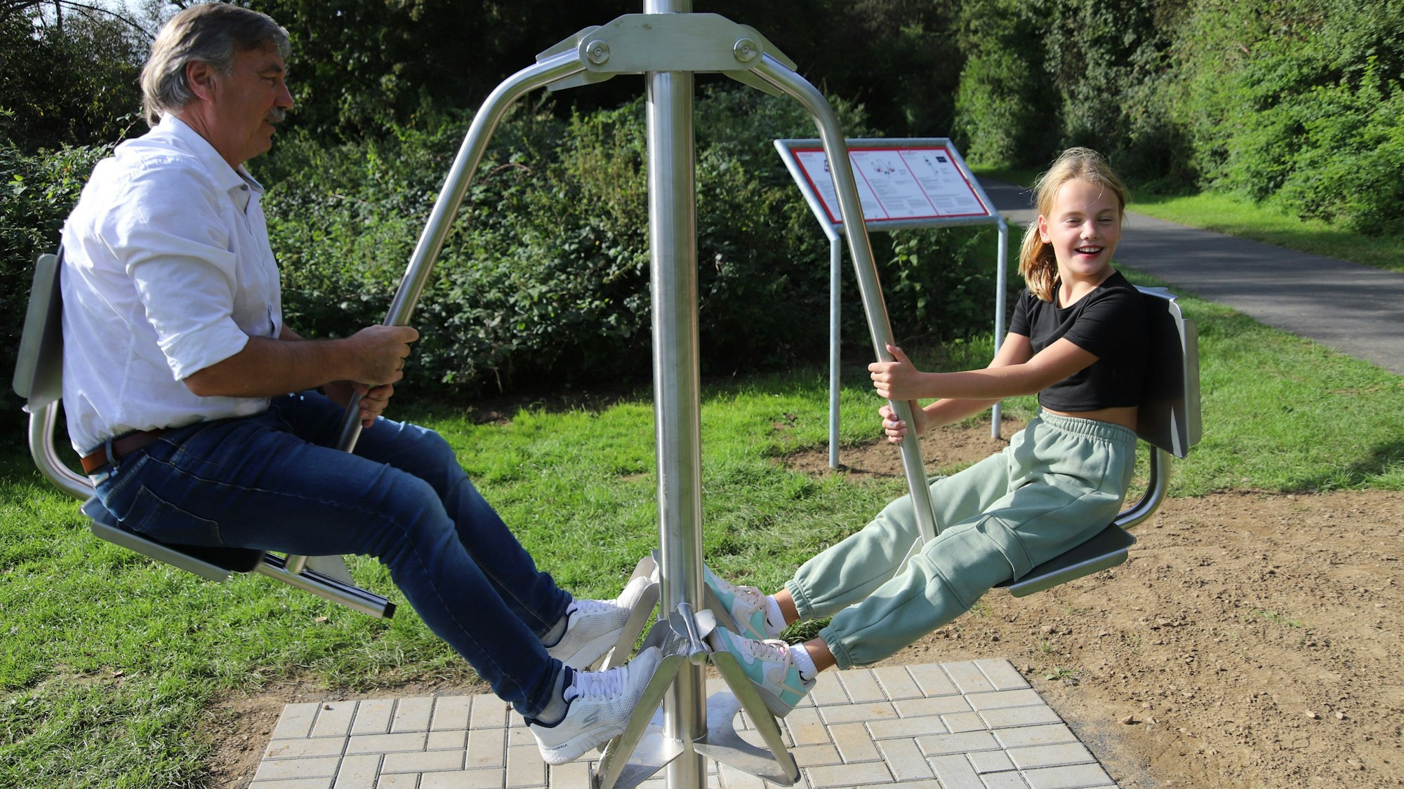 Ein Mann und ein junges Mädchen sitzen auf zwei beinlosen Stühlen, die an einem Metallarm hängen.