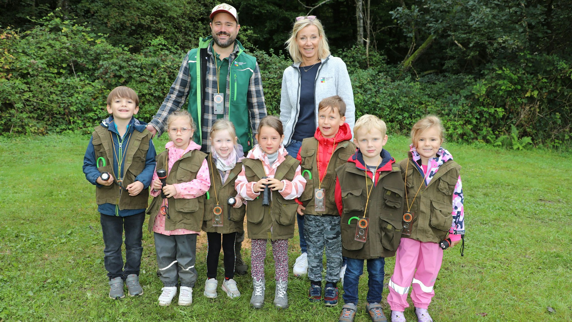 Eine Kindergruppe in Entdecker-Westen steht mit zwei Erwachsenen auf einer Wiese.
