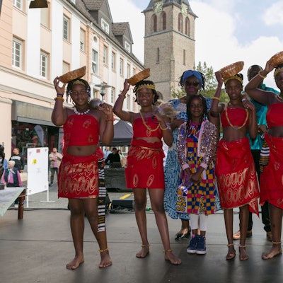 Frauen und Mädchen in bunten Kleidern posieren auf der Bühne auf dem Gummersbacher Lindenplatz, im Hintergrund die katholische Kirche.