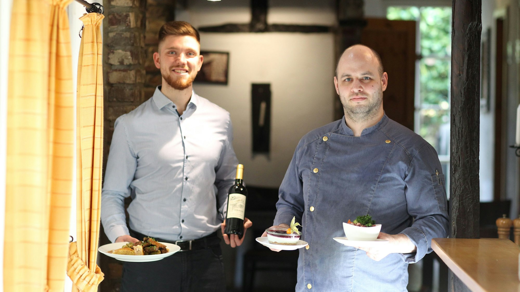 Zwei Männer präsentieren angerichtete Teller in einem Restaurant.