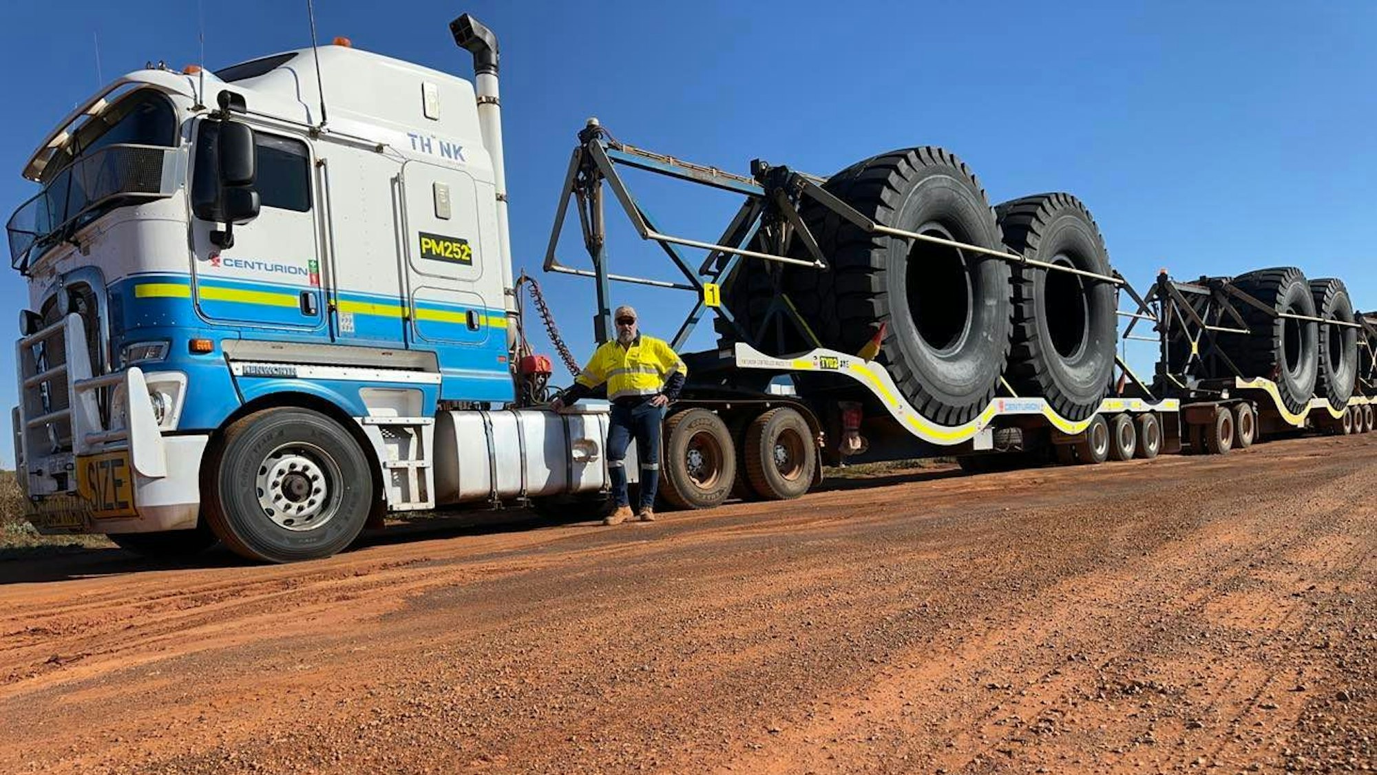 HANDOUT - 26.08.2023, Australien, Paynes Find: Der deutsche Fernlastfahrer Ingo Zacharias steht vor seinem «Road Train», mit dem er riesige Reifen 1600 Kilomater durch Australien transportiert. Der 53-Jährige aus Pulheim bei Köln befördert Güter über extrem weite Strecken mit seinem Mega-Laster. Die Gefährte sind so lang, dass der Vergleich mit einem Zug tatsächlich nahe liegt - oft messen sie mehr als 50 Meter. (zu dpa-Korr "Mit dem Mega-Truck durch Australien: Deutscher lebt Kindheitstraum") Foto: Ingo Zacharias/dpa - ACHTUNG: Nur zur redaktionellen Verwendung im Zusammenhang mit der aktuellen Berichterstattung und nur mit vollständiger Nennung des vorstehenden Credits +++ dpa-Bildfunk +++