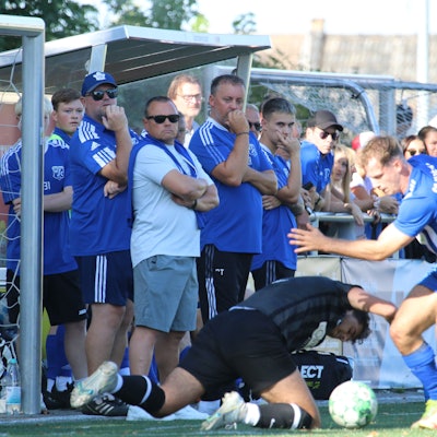 Ein Zweikampf, wobi ein Spieler auf dem Boden fällt, wird von der Auswechselbank verfolgt.