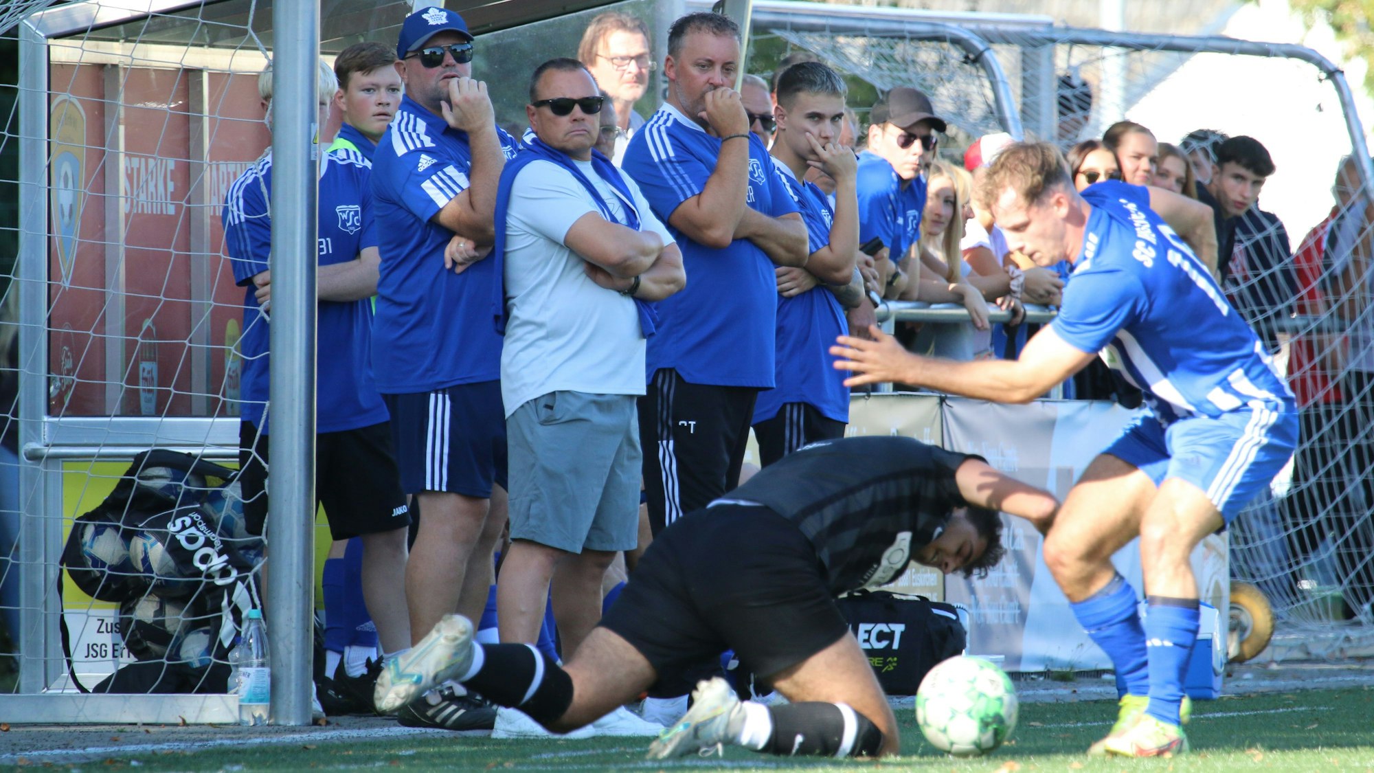 Ein Zweikampf, wobi ein Spieler auf dem Boden fällt, wird von der Auswechselbank verfolgt.
