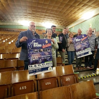 Im Kulturkino in Vogelsang machen Organisatoren und Akteure Werbung für das Weihnachtsprogramm der Bundeswehr-Bigband. Einige halten Plakate in den Händen.